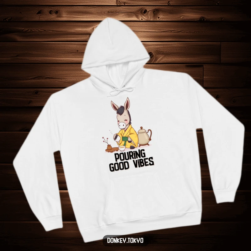 Funny donkey in a yellow kimono gently pouring tea, printed on a cozy hoodie for humorous warmth and calm.